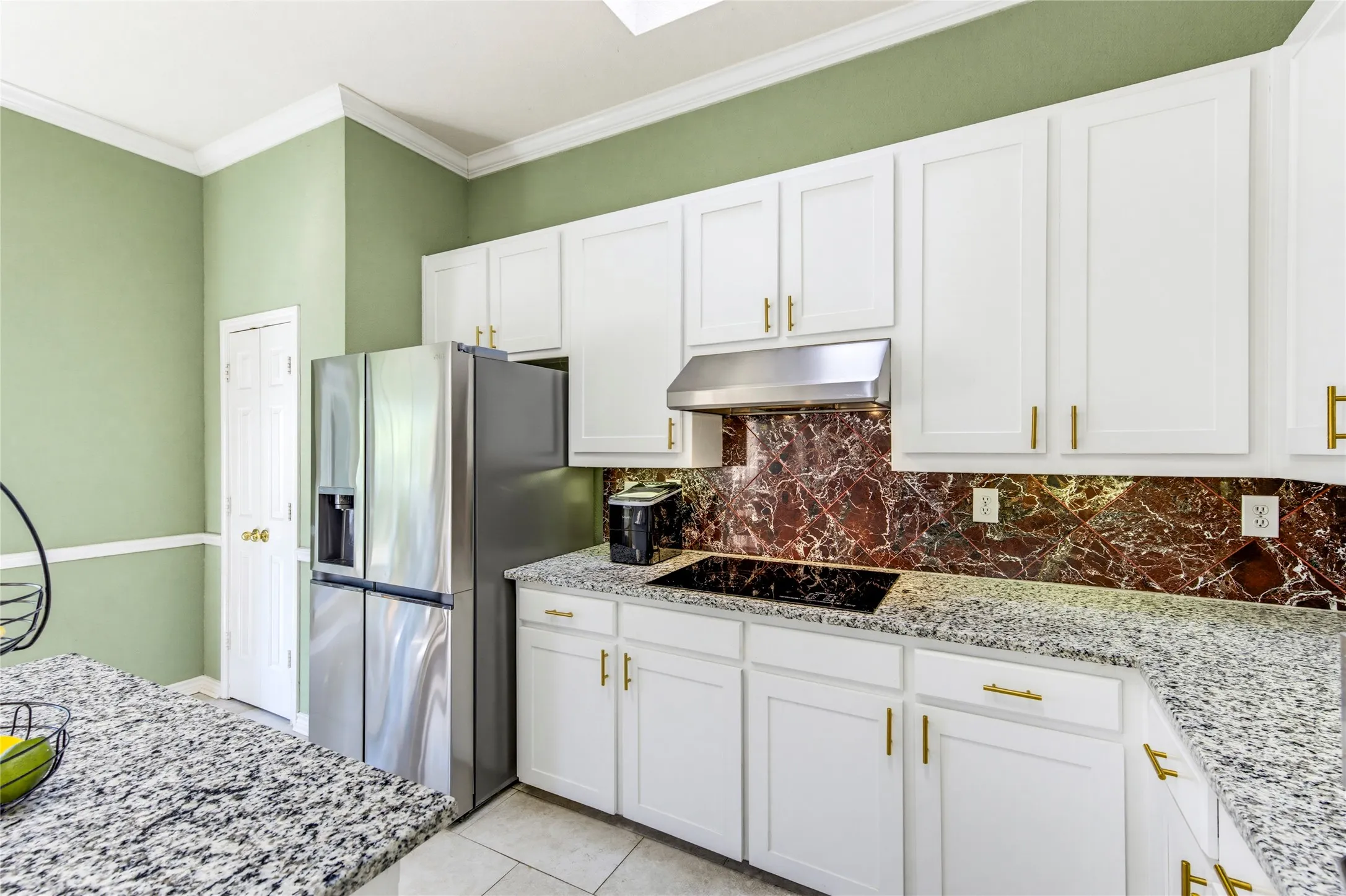 White cabinetry with gold-tone hardware, granite countertops, and a full-height marble backsplash and pantry in the corner....