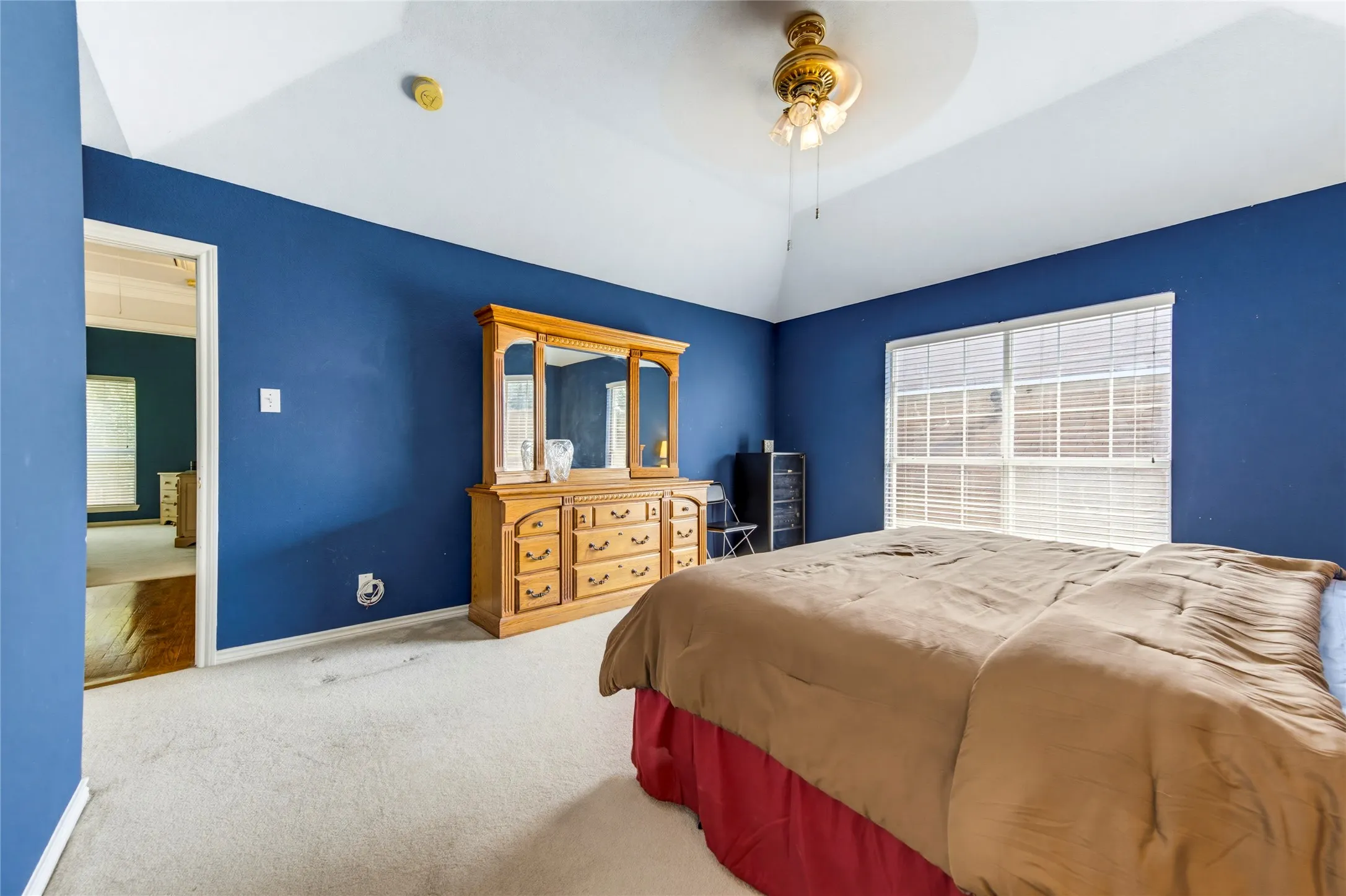 Vaulted ceiling with an attached ceiling fan, carpeted flooring, large window with blinds, and painted walls
