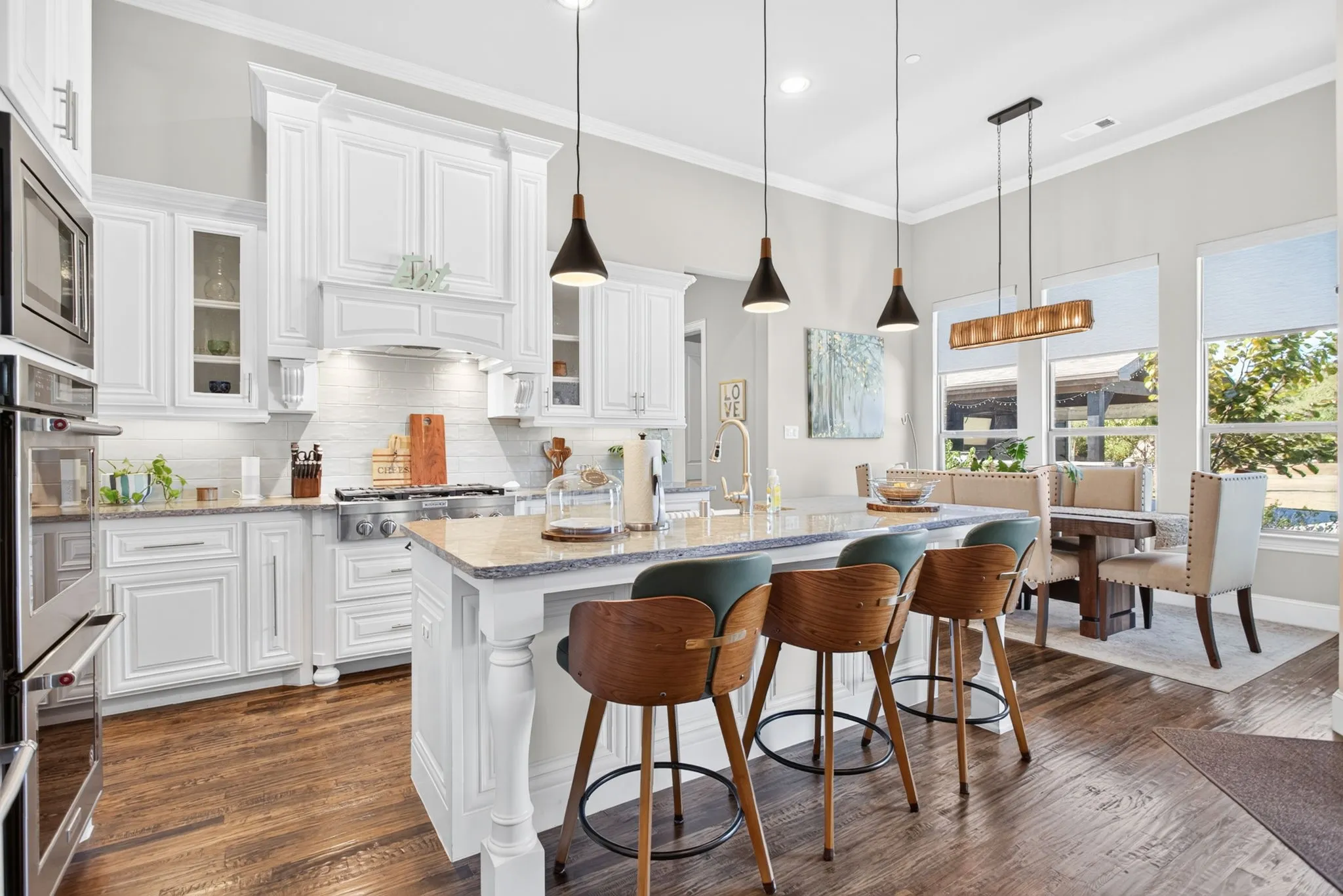 Gourmet kitchen featuring white cabinetry, stainless steel appliances, a large island with seating, wood-finish flooring, and ample natural light