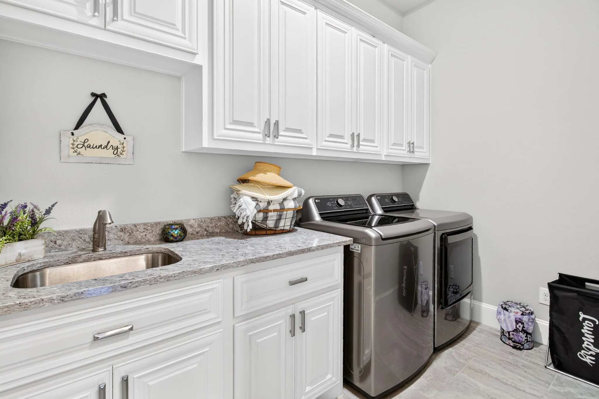 White shaker-style cabinetry with crown molding, undermount sink, stone countertop, and tile flooring