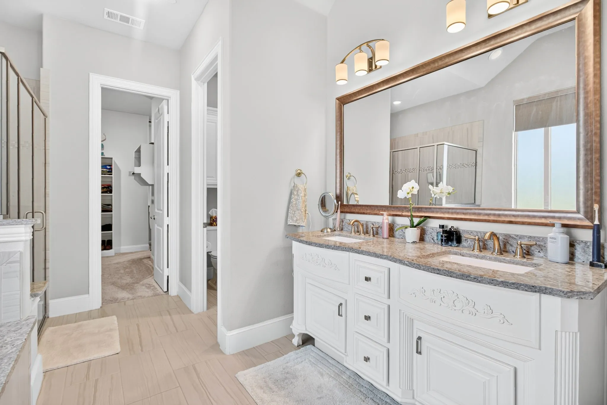 Dual vanity with integrated sinks, granite countertop, ornate white cabinetry, and a large framed mirror