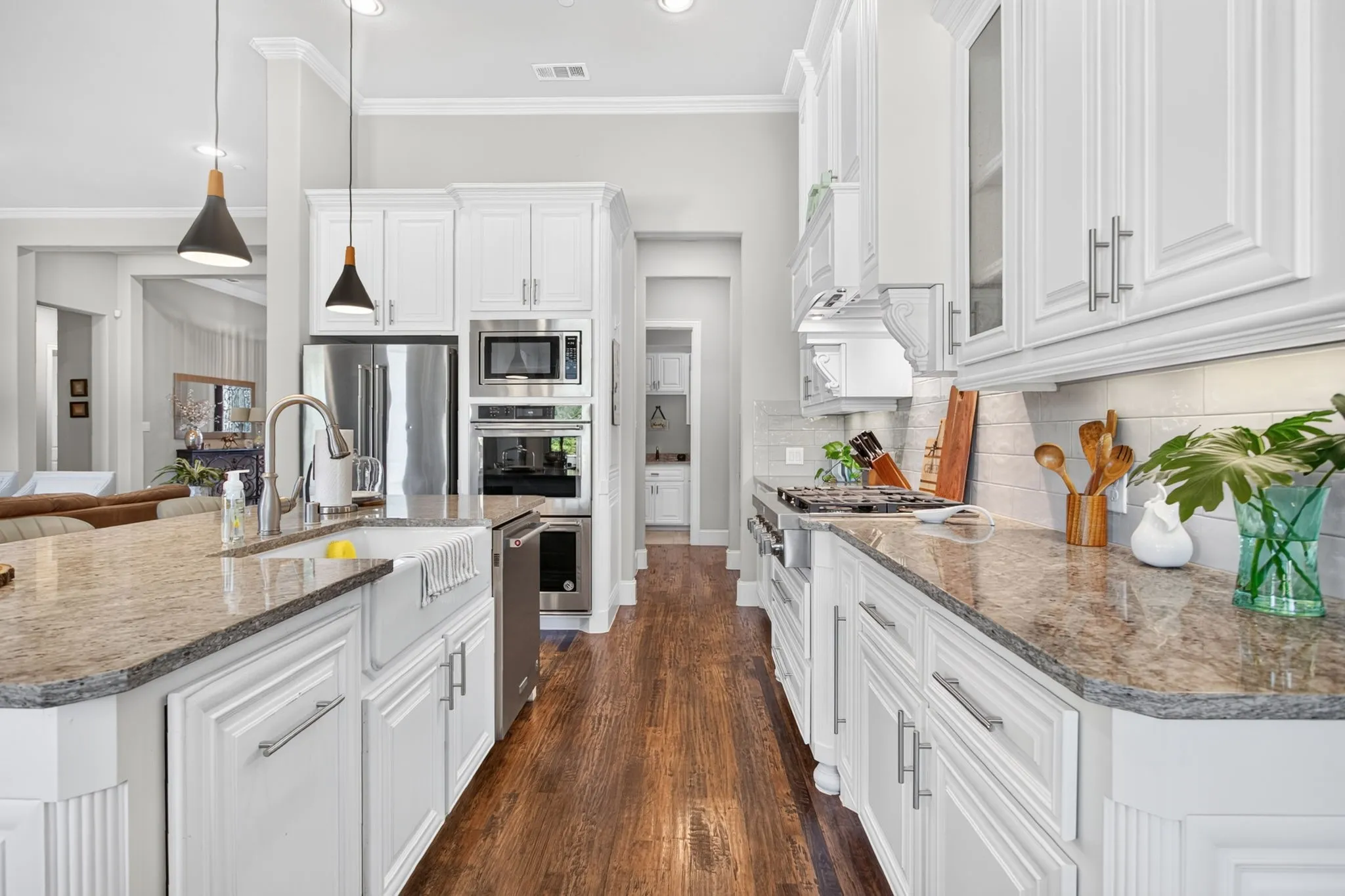 Gourmet kitchen featuring white cabinetry, stone countertops, wood-finish flooring, stainless steel appliances, and a farmhouse sink