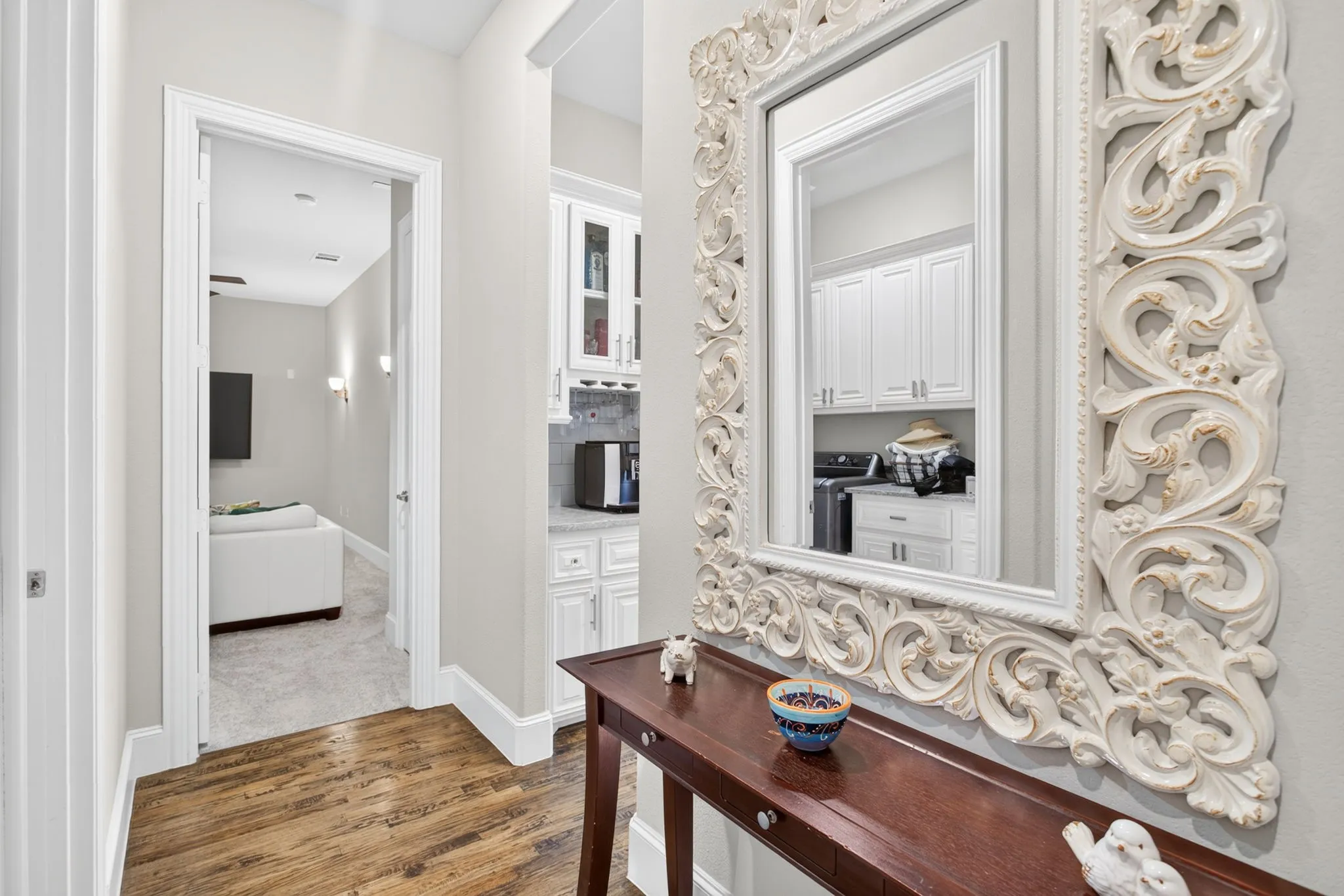 Wood-finish flooring with white trim, a built-in wet bar featuring white cabinetry and a tile backsplash, and a separate room with carpeted flooring