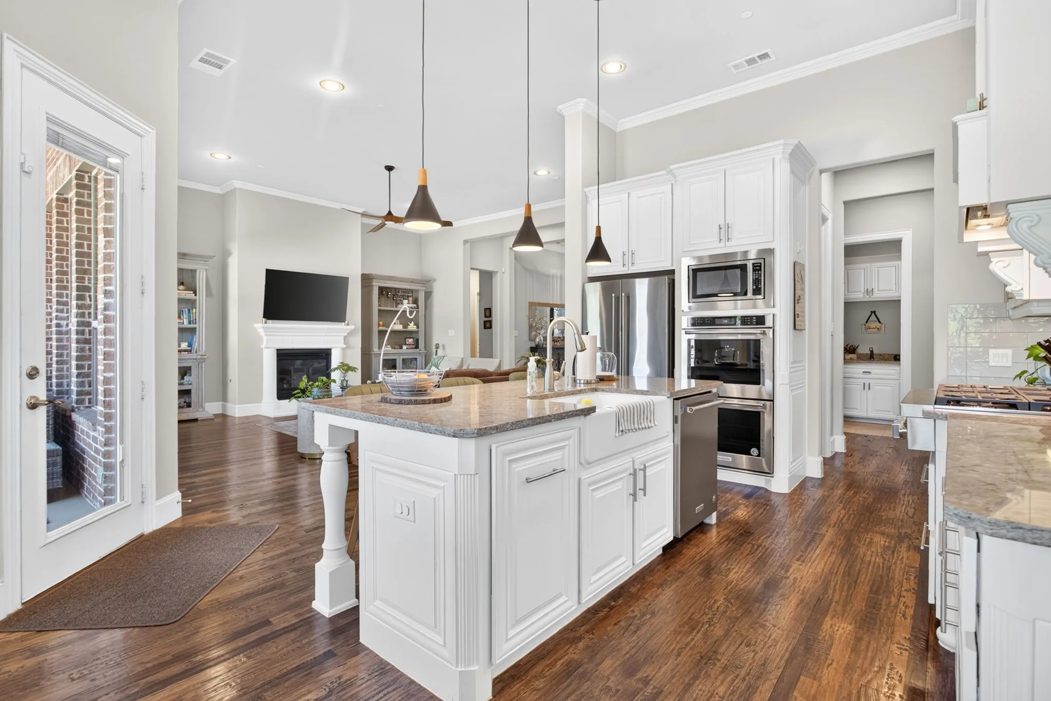 Kitchen island with a farmhouse sink, stainless steel appliances, wood-finish flooring, white cabinetry, and a fireplace in the background