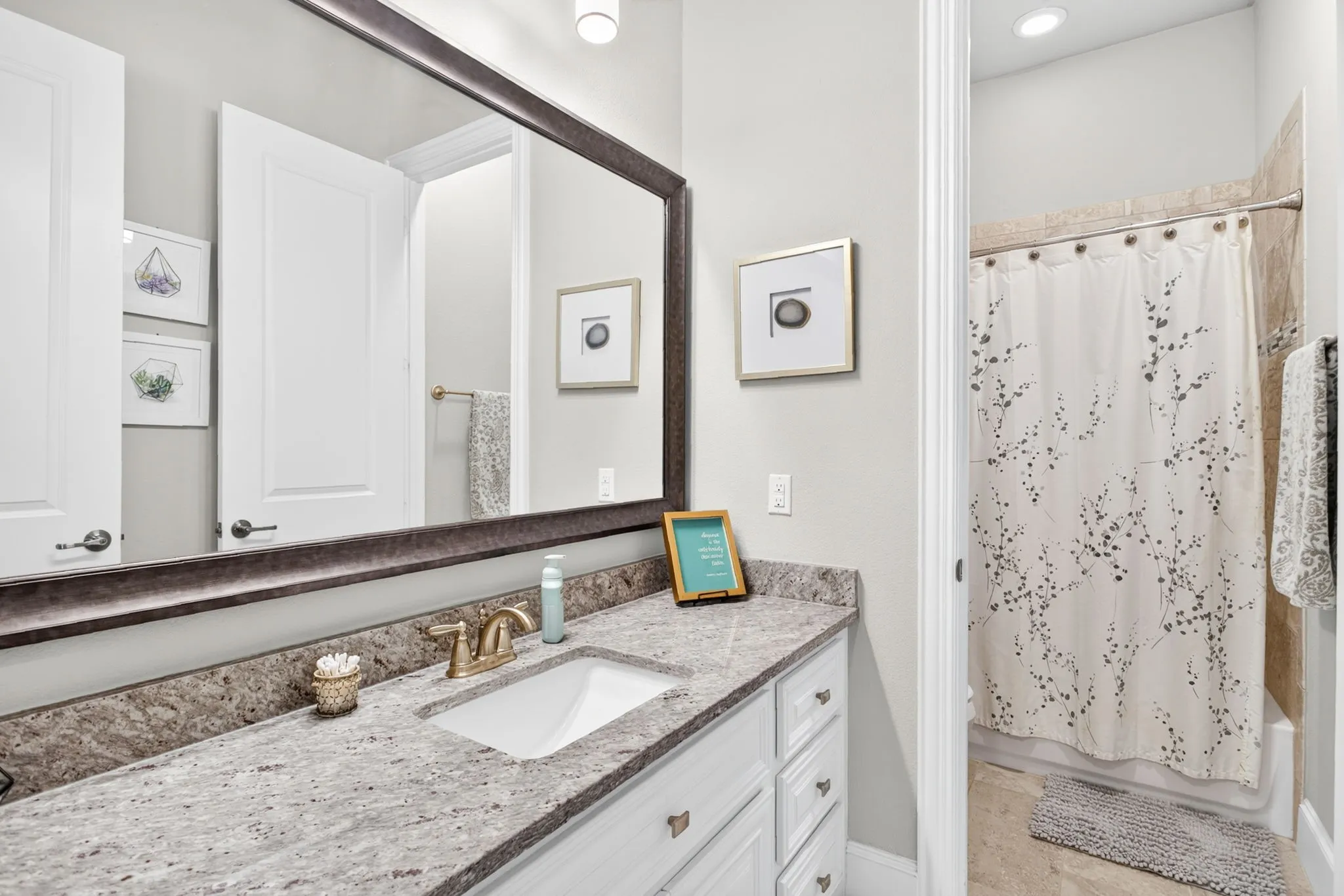 Vanity with a substantial framed mirror, a single integrated sink, a granite countertop, and white cabinetry with drawer storage