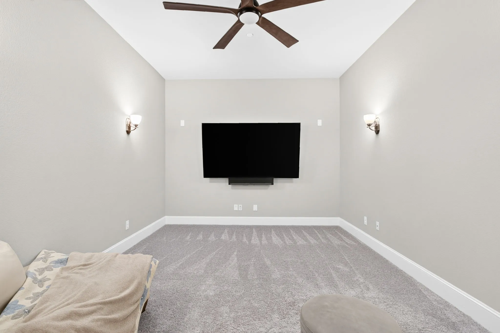 Carpeted flooring, mounted television, ceiling fan, and wall sconces