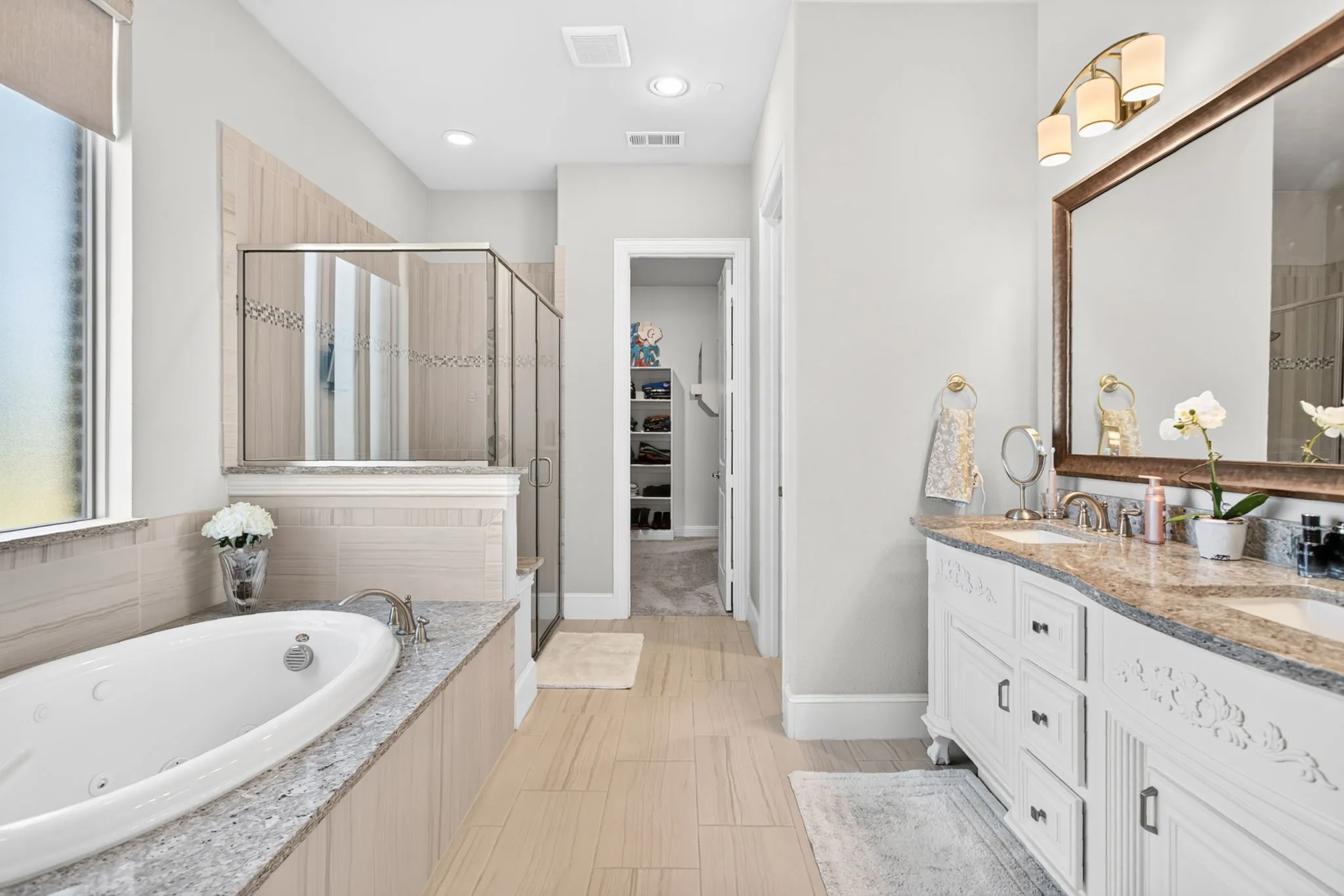 Dual vanity with granite countertop, built-in soaking tub, glass-enclosed shower, and tile flooring