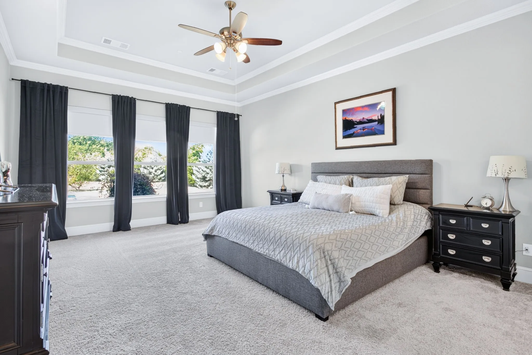 Tray ceiling with crown molding, ceiling fan, and light-toned carpet flooring