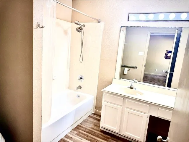 Tub and shower combination with chrome fixtures, wood-finish flooring, white vanity with integrated sink, and an overhead vanity light fixture