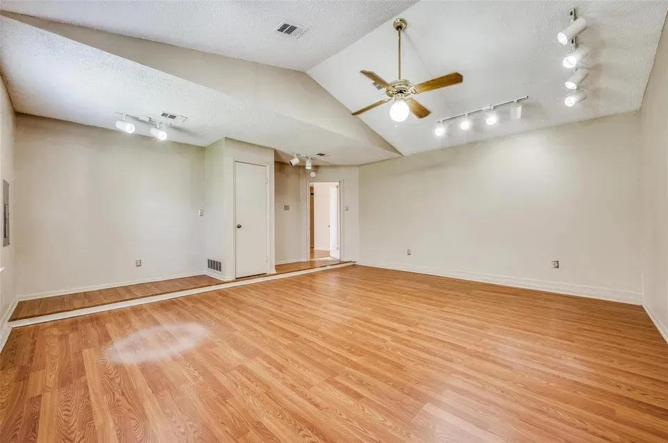 Wood-finish flooring, vaulted ceiling, ceiling fan, track lighting, and neutral wall tones