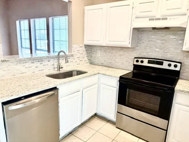 White cabinetry, granite countertops, tile backsplash, stainless steel sink with gooseneck faucet, and stainless steel dishwasher