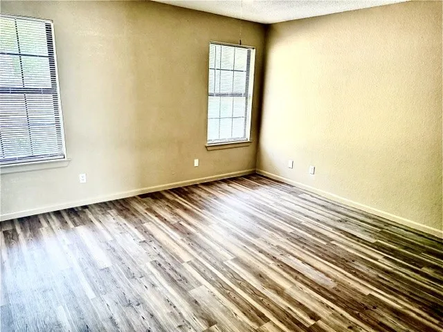 Spacious room featuring wood-finish flooring, light-toned walls, and multiple windows with blinds