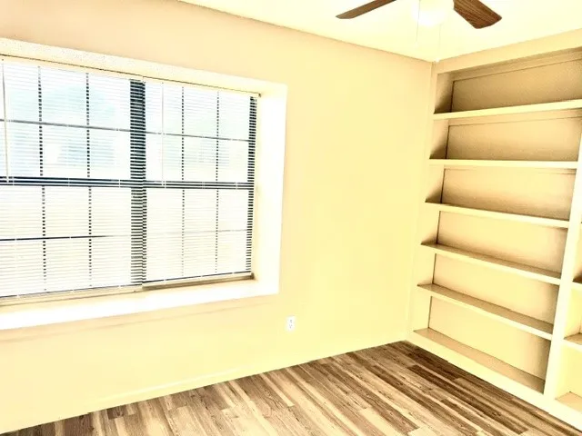 Wood-finish flooring, built-in shelving, window with blinds, and ceiling fan