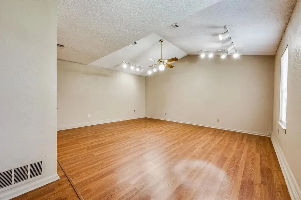 Vaulted ceiling with a ceiling fan, wood-finish flooring, and track lighting fixtures
