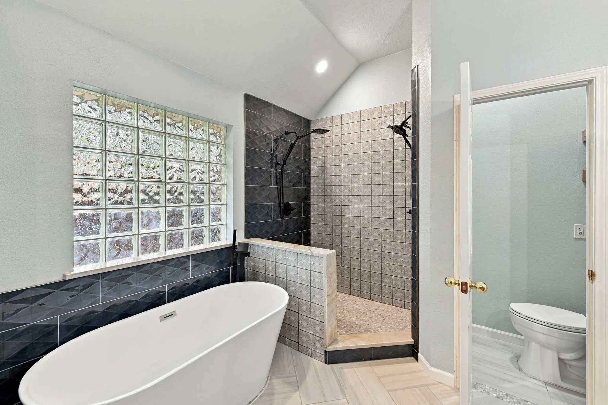 Freestanding soaking tub, glass block window, walk-in shower with dual shower heads, and light-toned flooring