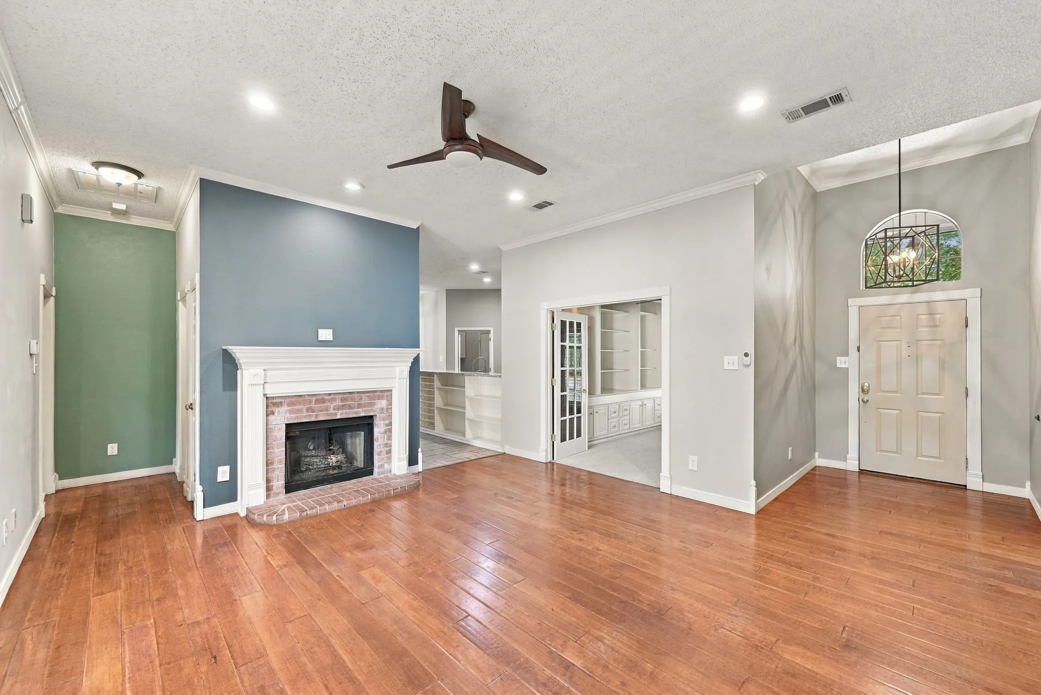 Hardwood flooring, brick fireplace with mantel, recessed lighting, ceiling fan, and French doors leading to a separate room with built-in shelving