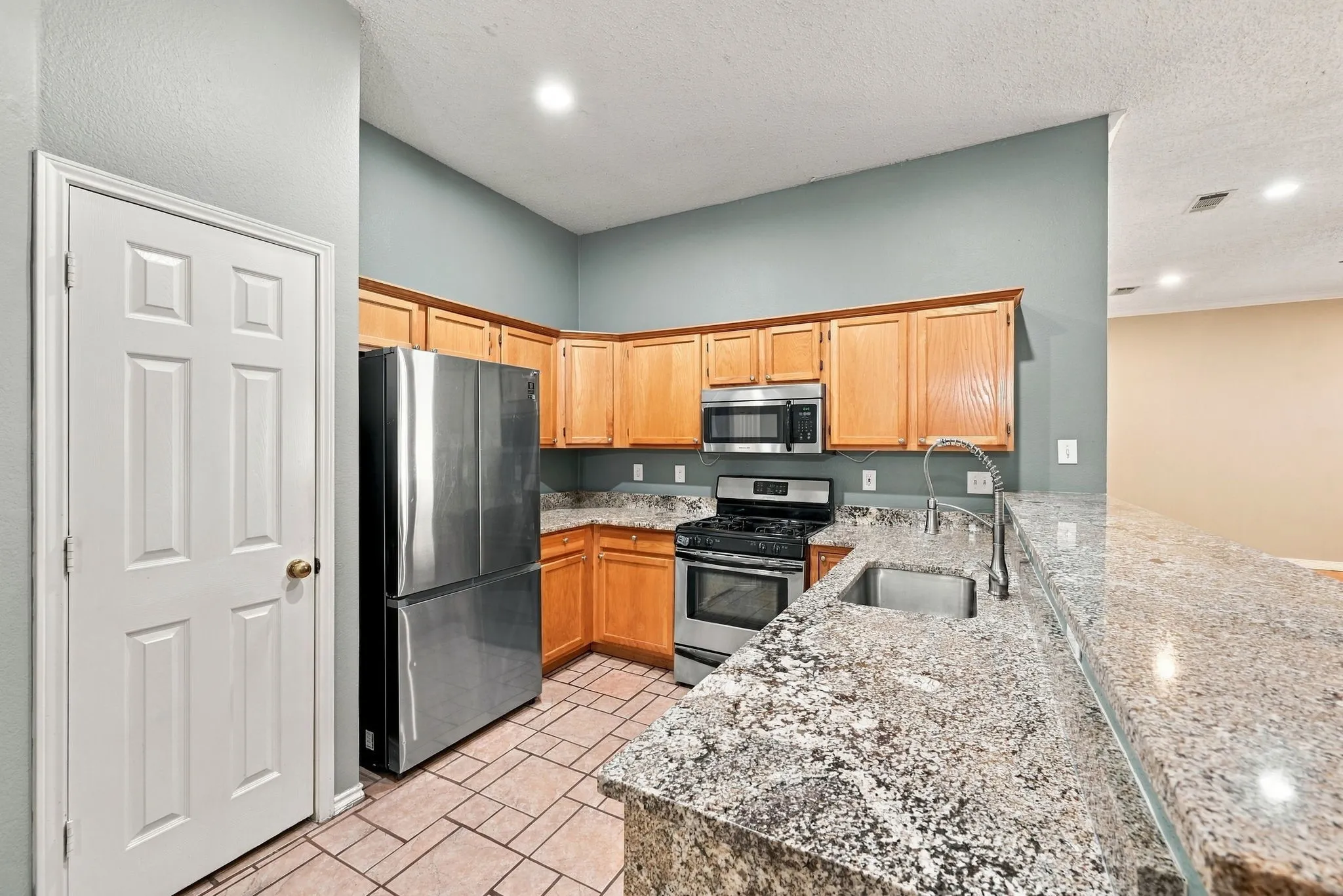 Kitchen featuring wood cabinetry, stainless steel appliances, granite countertops, and tile flooring