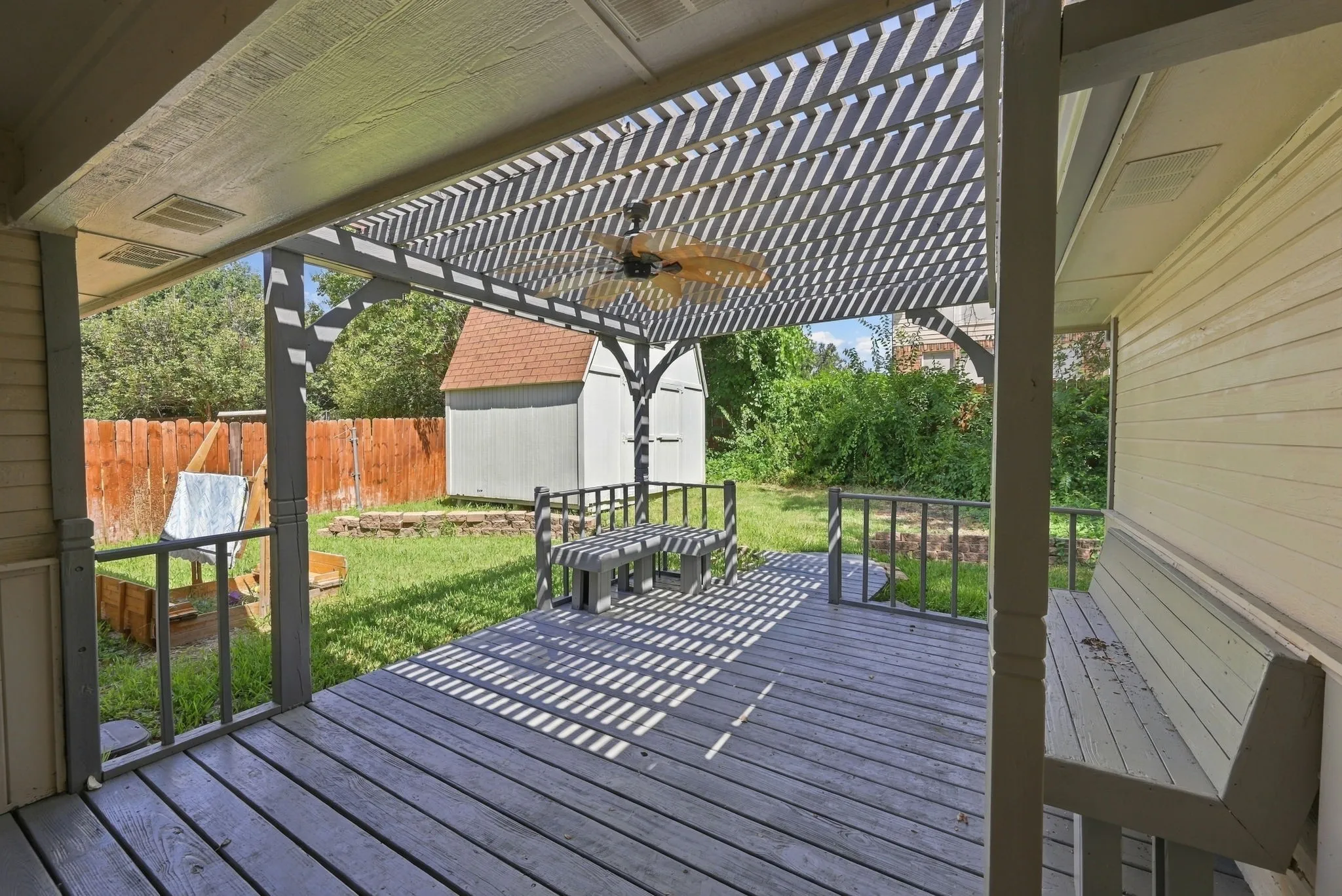Decked patio with a slatted pergola, ceiling fan, and built-in bench seating