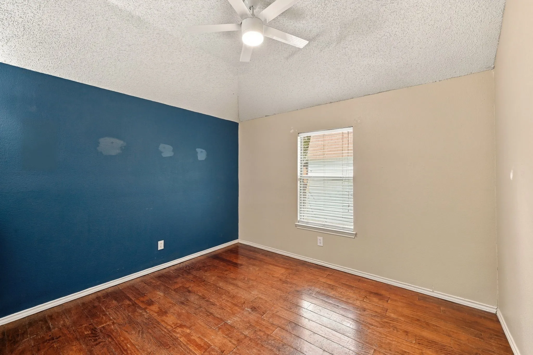 Vaulted ceiling with an attached ceiling fan, rich wood-finish flooring, and a window with blinds