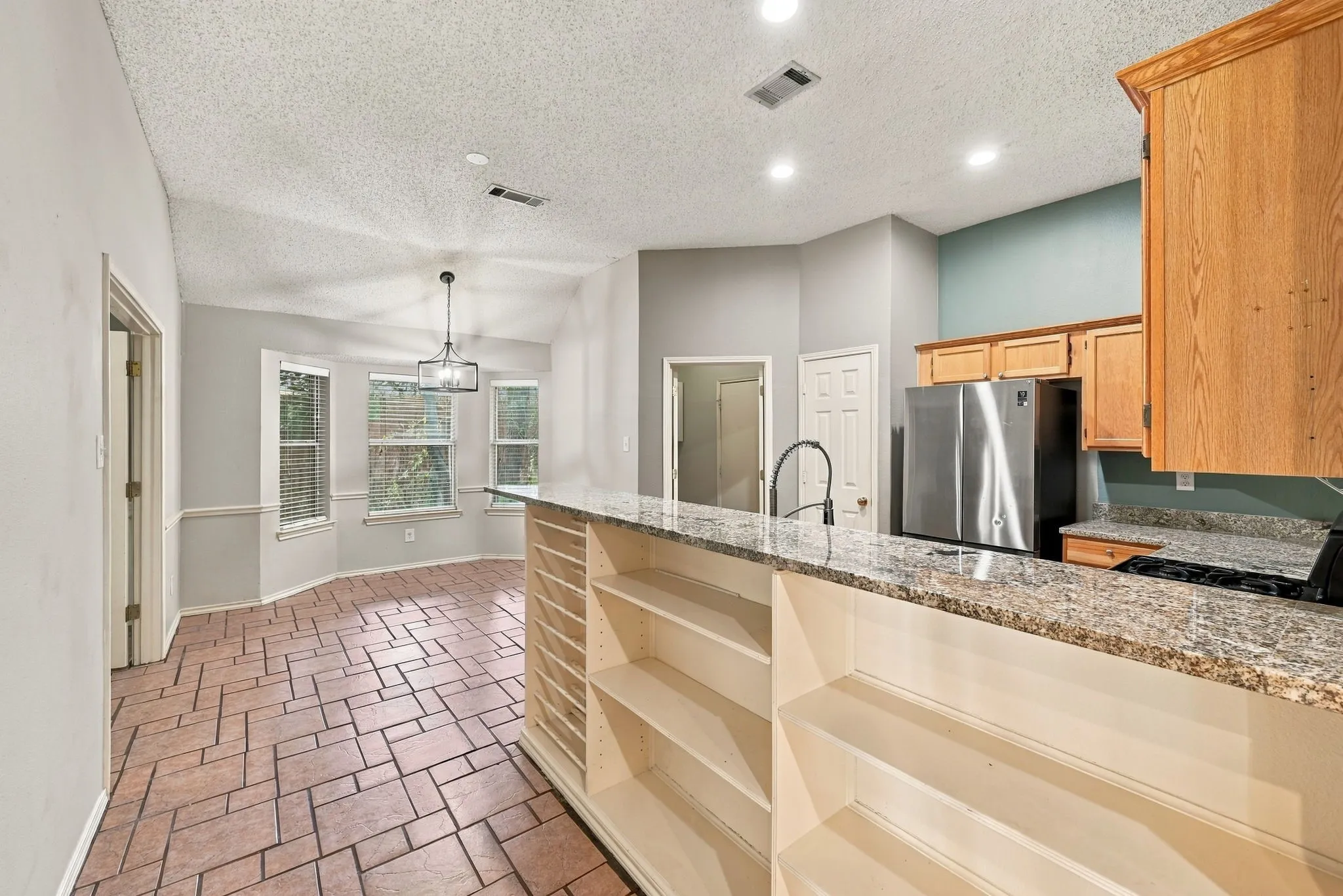 Kitchen featuring a granite-finish countertop, wood-finish cabinetry, stainless steel refrigerator, and a gooseneck faucet