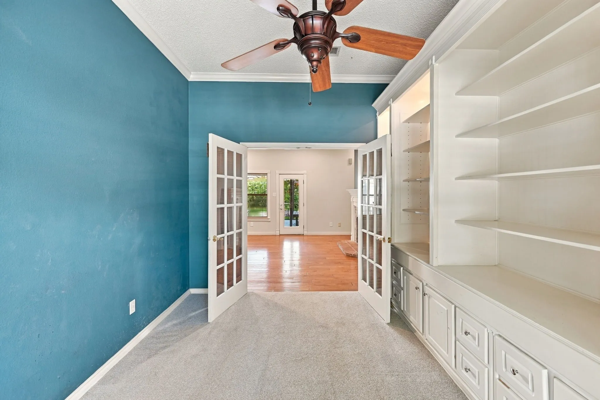 Built-in shelving with lower cabinetry, wood-finish ceiling fan, and double French doors with glass panes