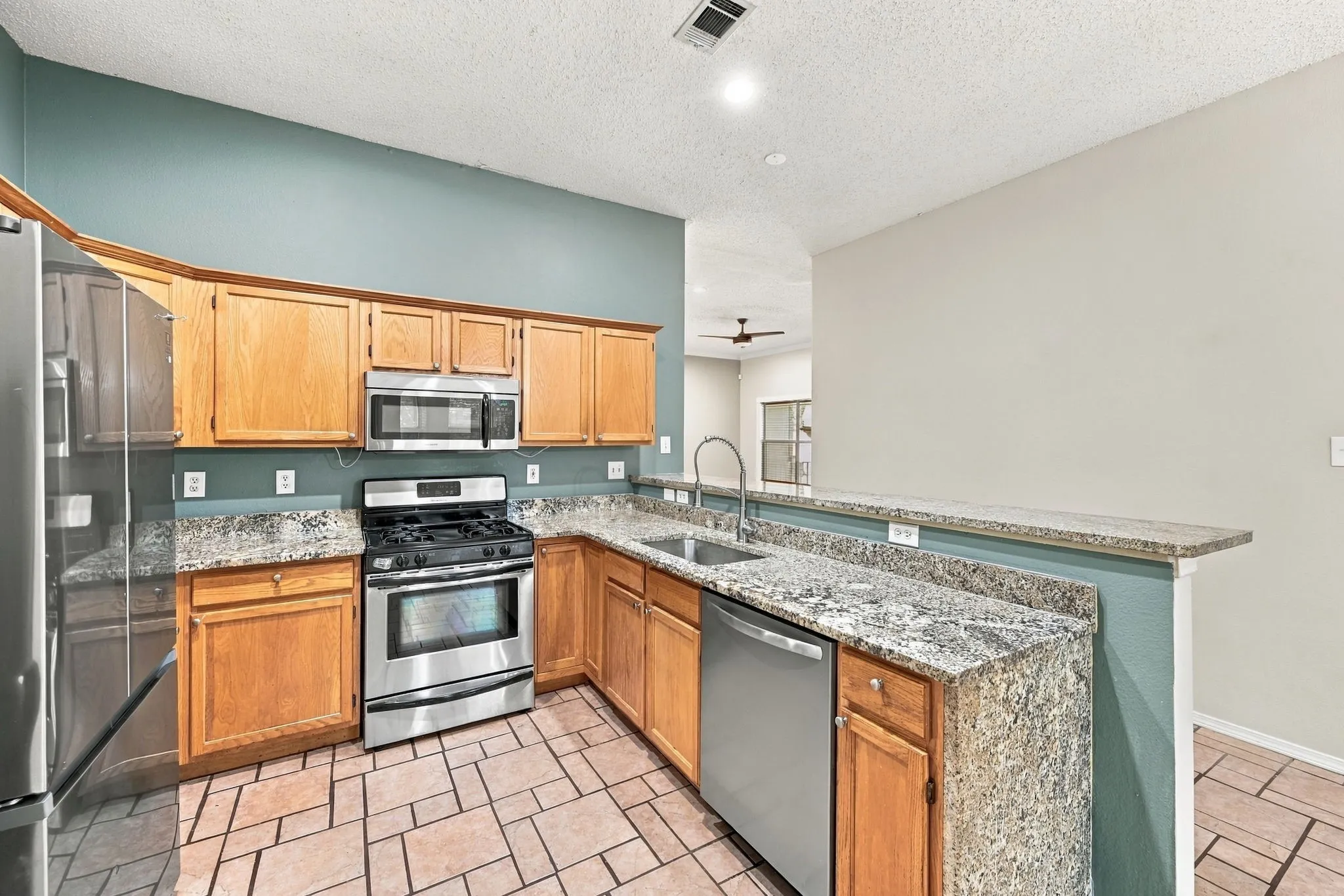Kitchen featuring stainless steel appliances, wood cabinetry, granite countertops, and tile flooring