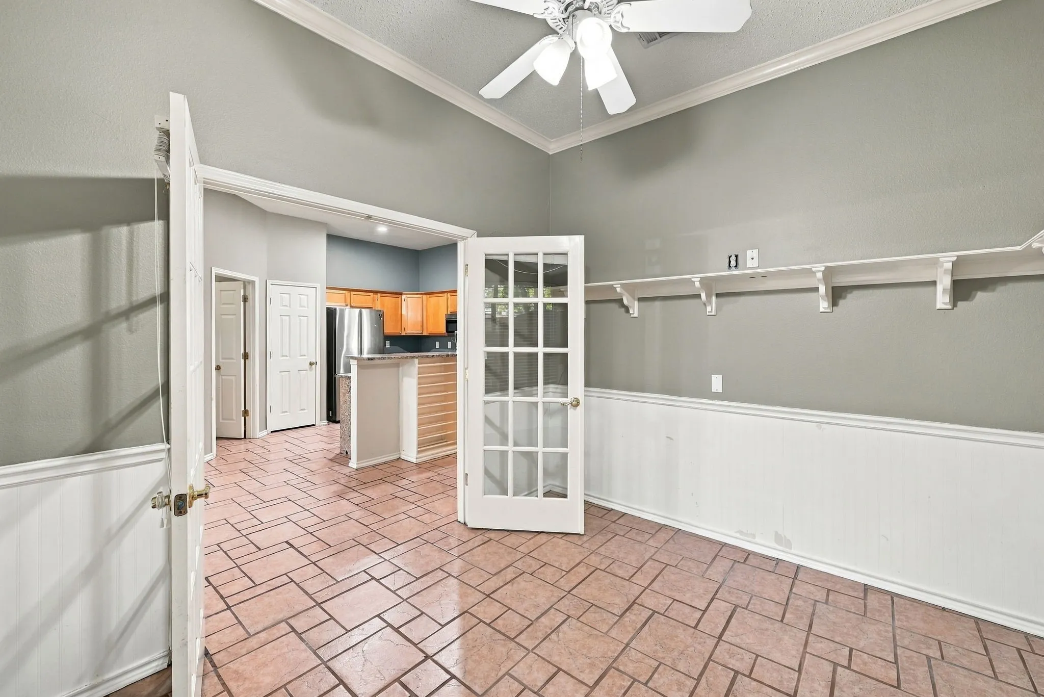 Vaulted ceiling with a ceiling fan, French doors with glass panels, tile flooring in a geometric pattern, and wainscoting