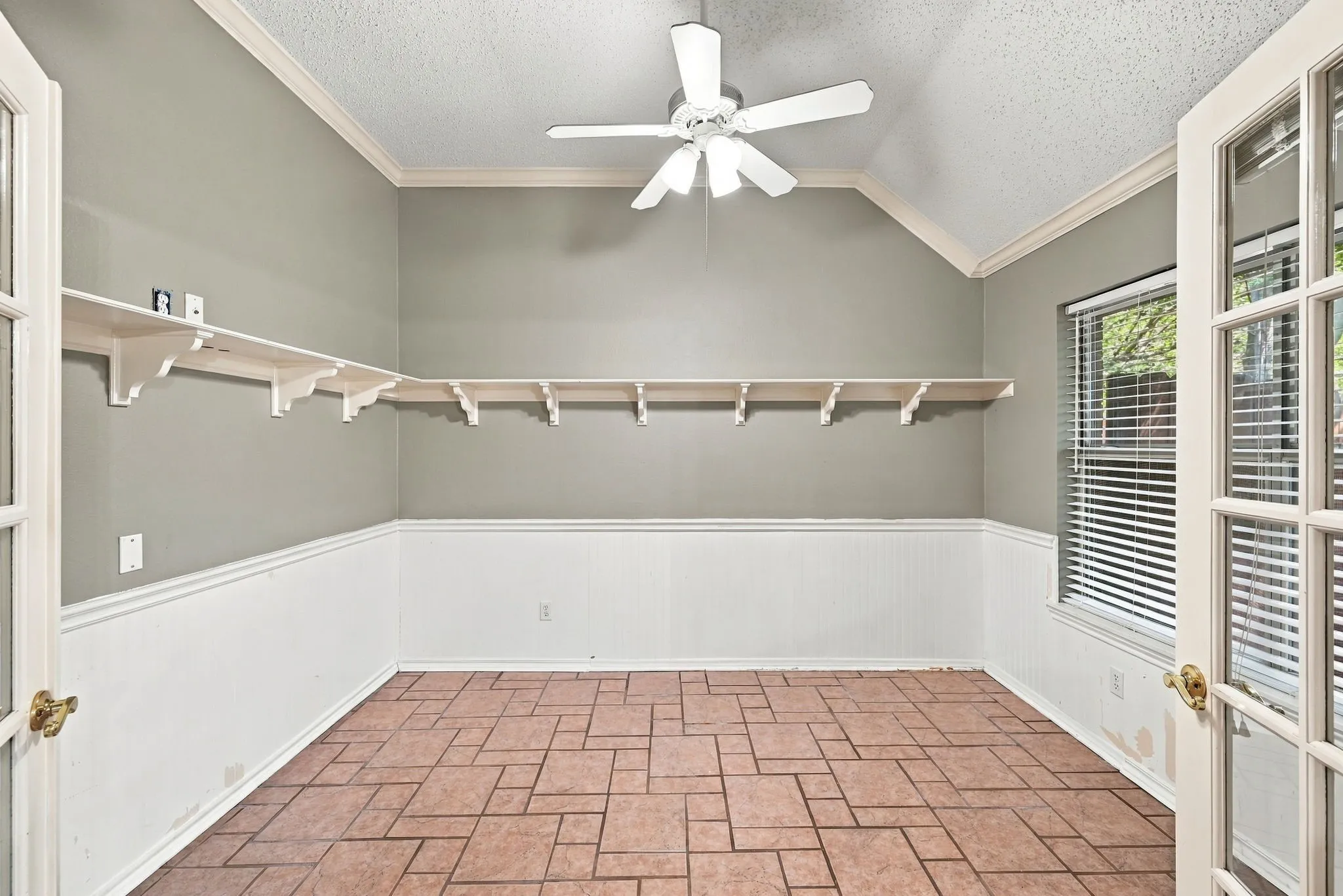 Vaulted ceiling with ceiling fan, wall-mounted shelving, wainscoting, and tile flooring