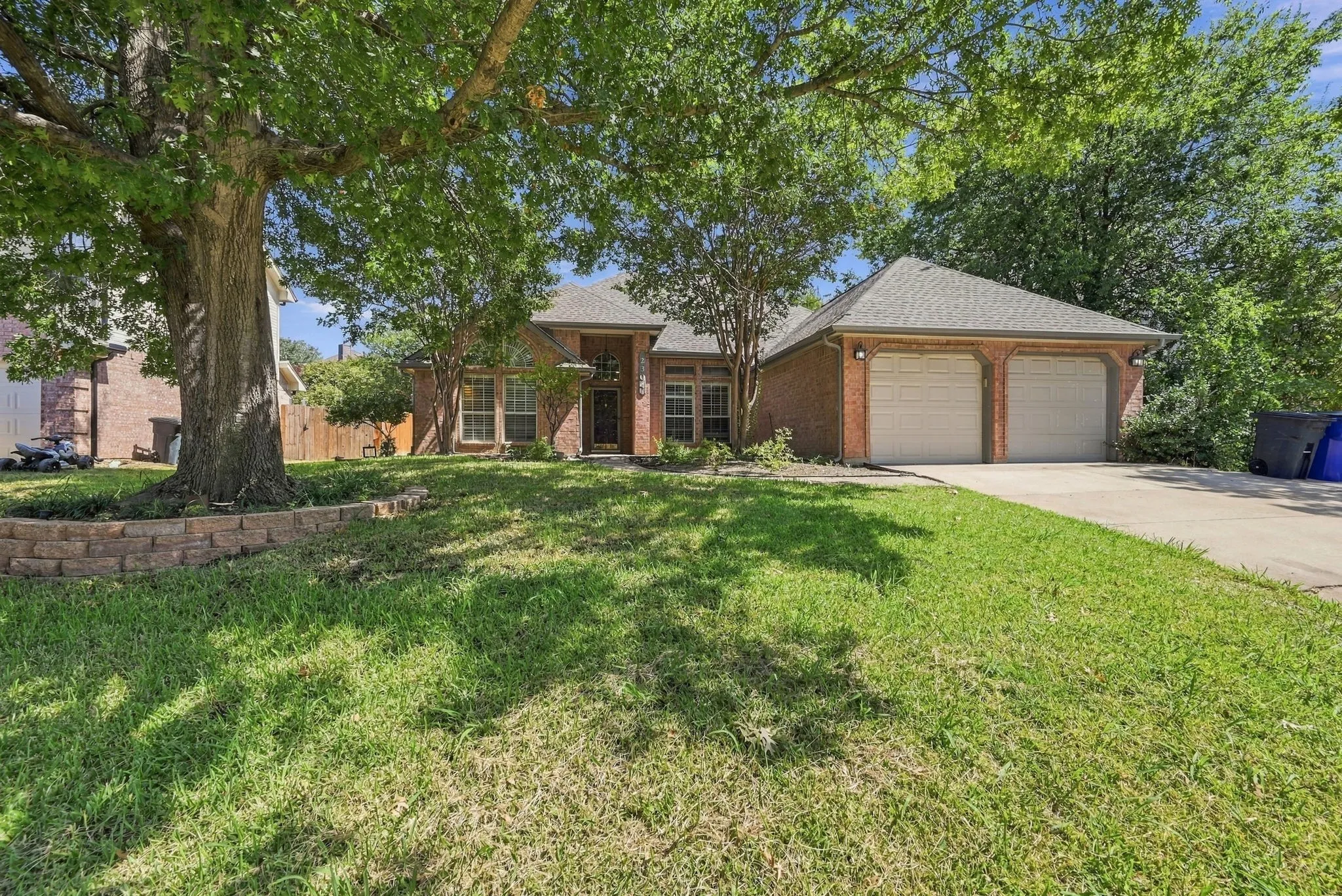 Brick exterior, two-car garage, mature trees, and a concrete driveway