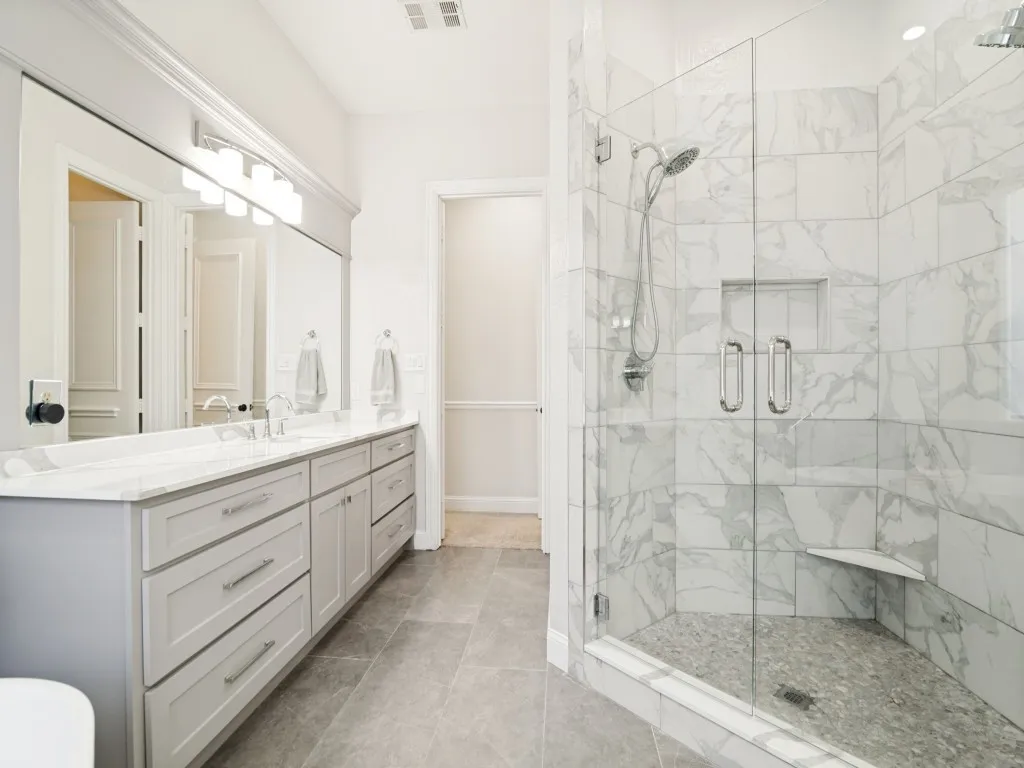 Beautiful master bath renovation completed in 2023 features separate vanities and oversized glass and tiled shower.