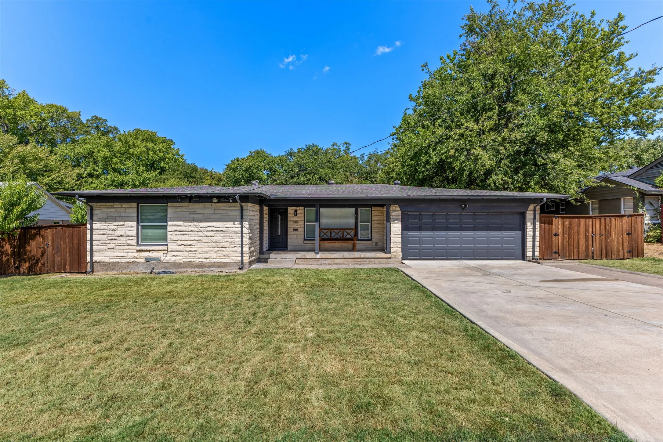 Stone veneer exterior with a dark garage door, concrete driveway, and a front lawn
