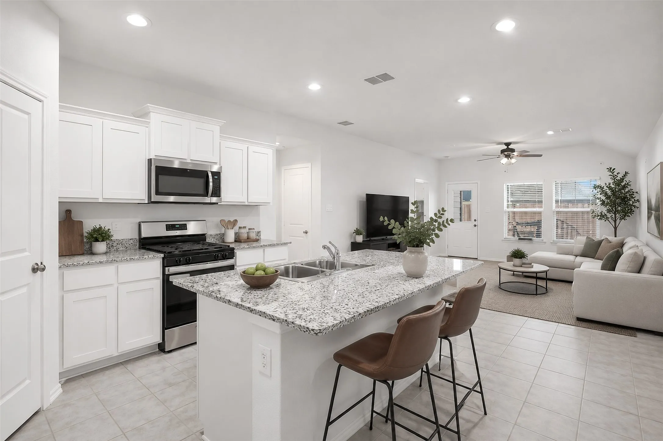 Open-concept living area featuring a kitchen island with seating, stainless steel appliances, white cabinetry, recessed lighting, and a vaulted ceiling