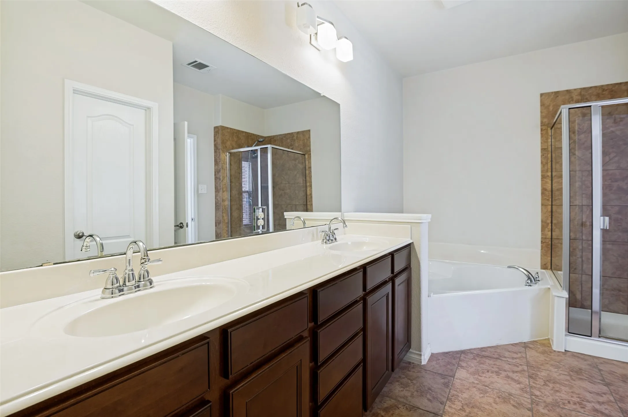 Dual master vanity with integrated sinks, full-width mirror, built-in bathtub, glass-enclosed shower, and tiled flooring