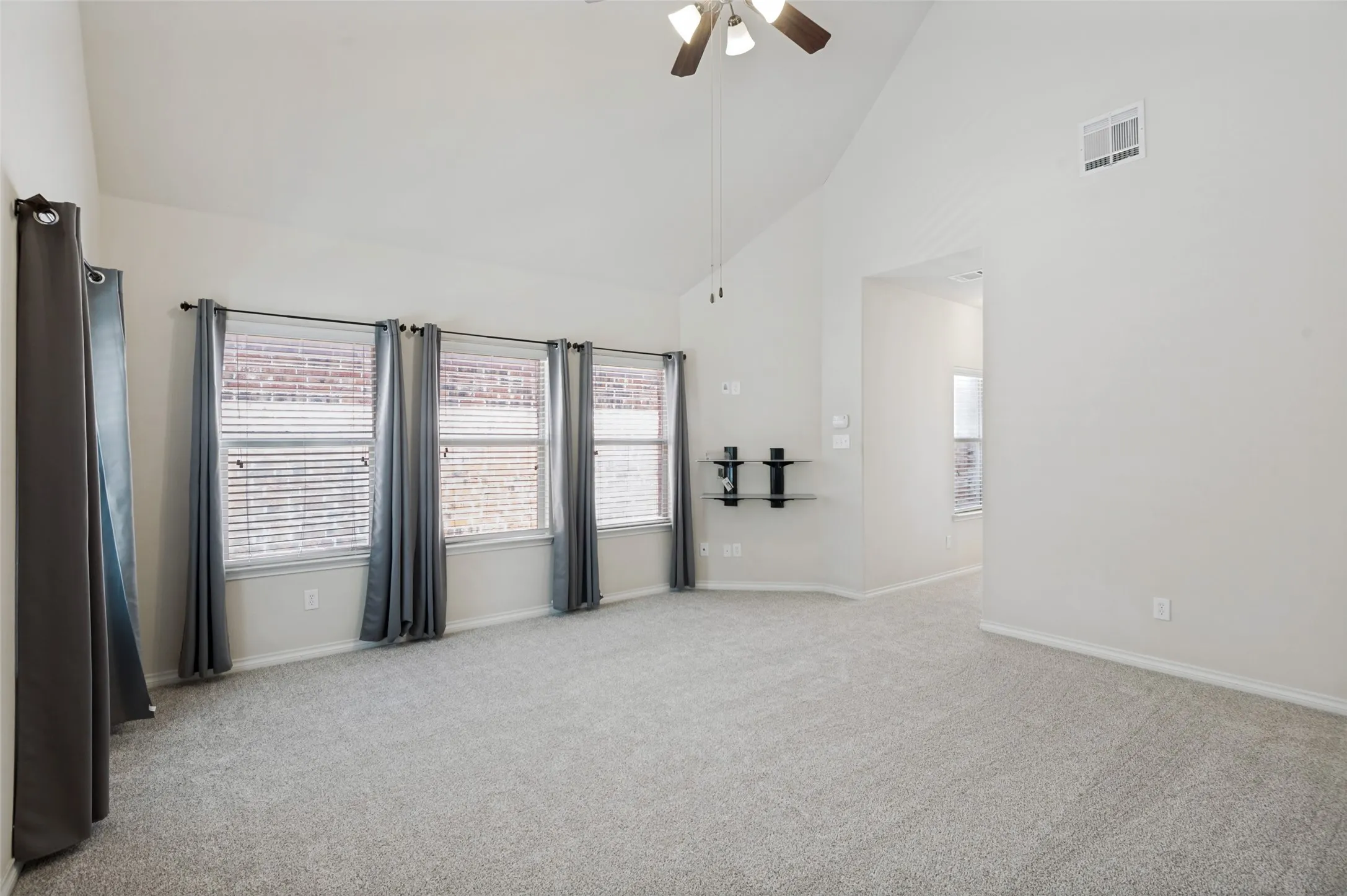 Huge Master Bedroom with vaulted ceiling, ceiling fan, three windows with blinds, wall-mounted shelving, and carpeted flooring