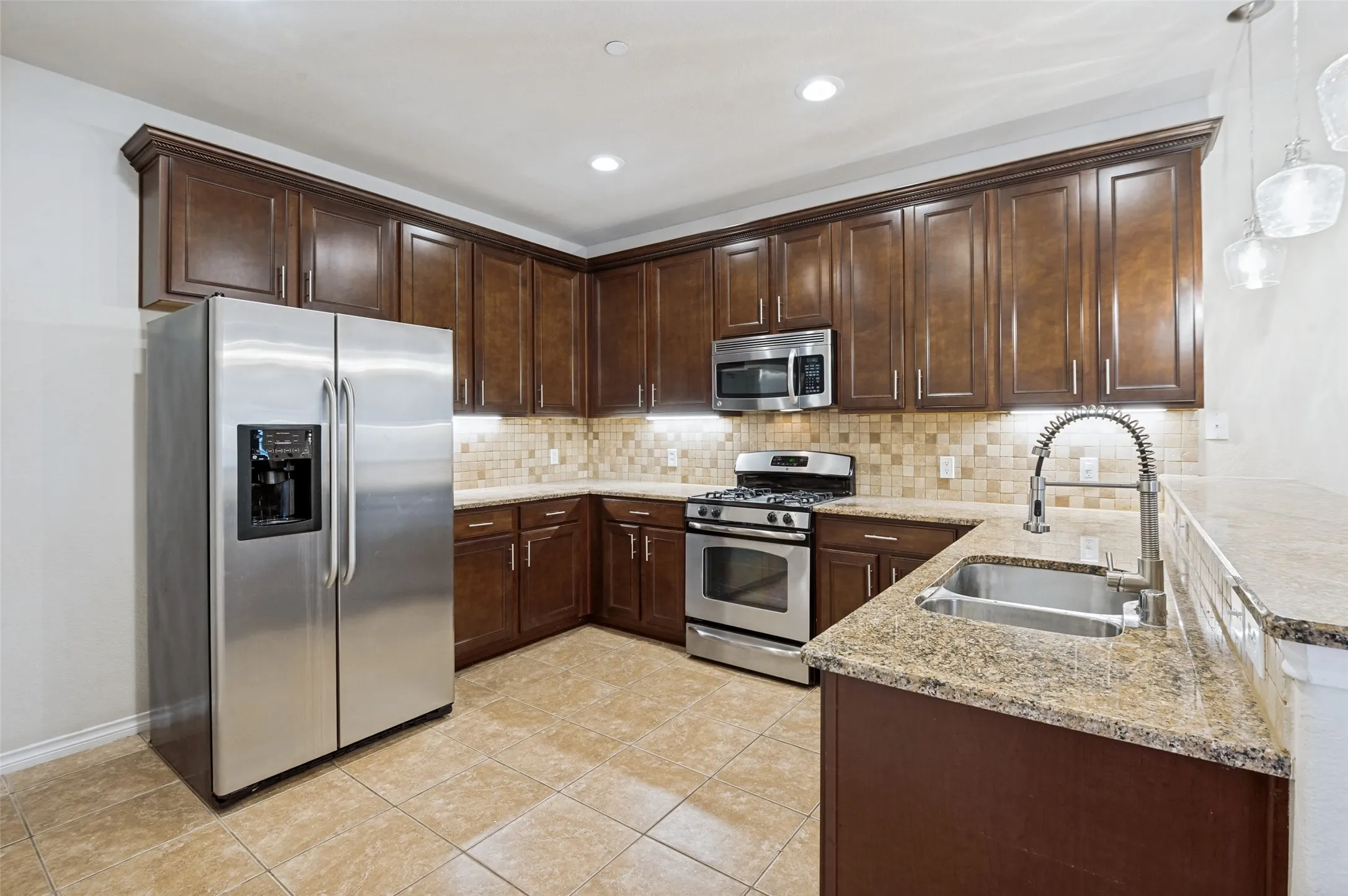 Kitchen featuring wood-finish cabinetry, stainless steel appliances, granite countertops, tile backsplash, and recessed lighting
