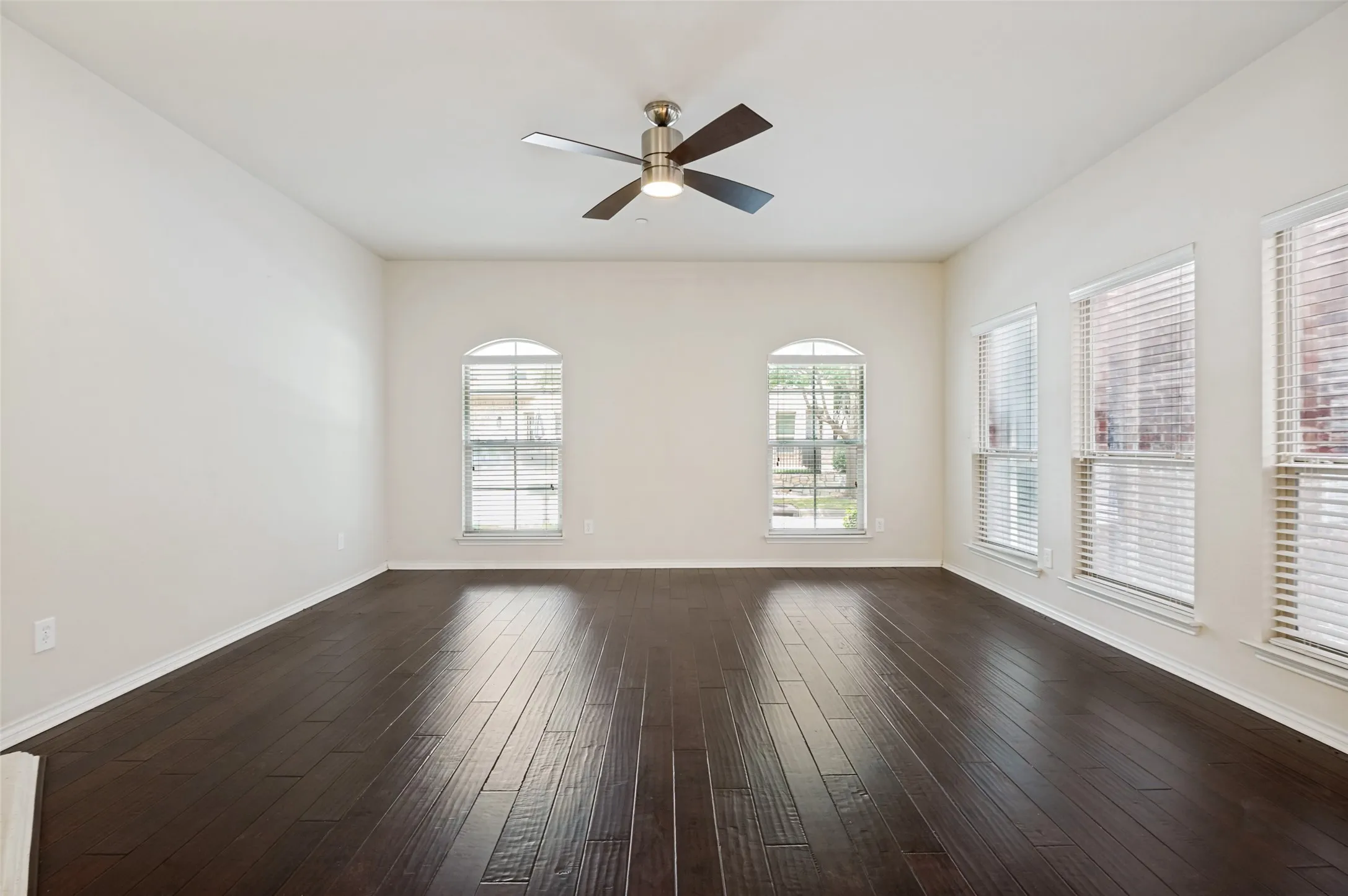 Wood-finish flooring, white walls, arched window, two rectangular windows, and a ceiling fan with light fixture