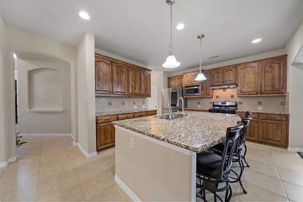 Kitchen featuring a central island with a sink, recessed lighting, wood-finish cabinetry, and stainless steel appliances