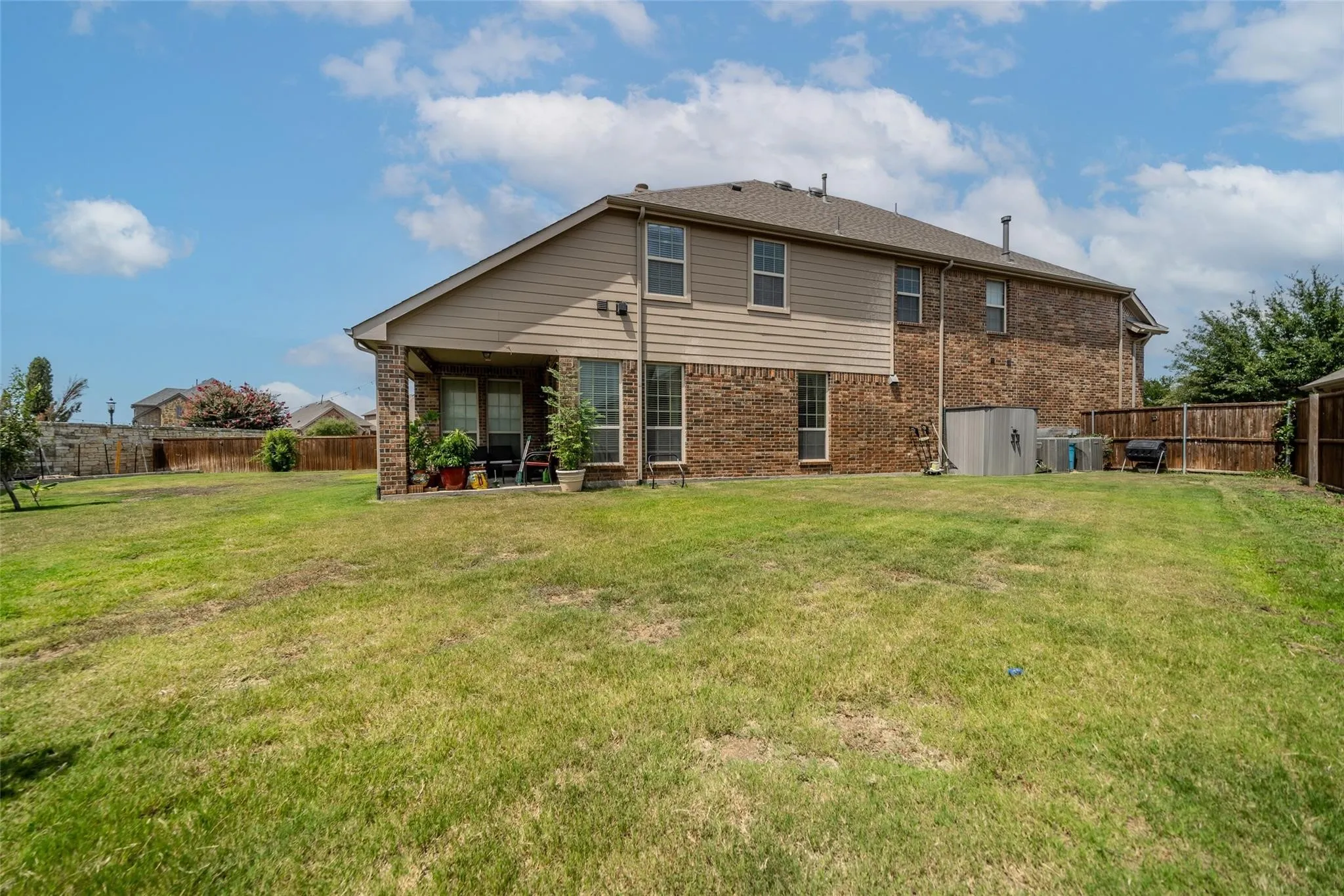 Expansive backyard featuring a covered patio, brick exterior, siding accents, and a privacy fence