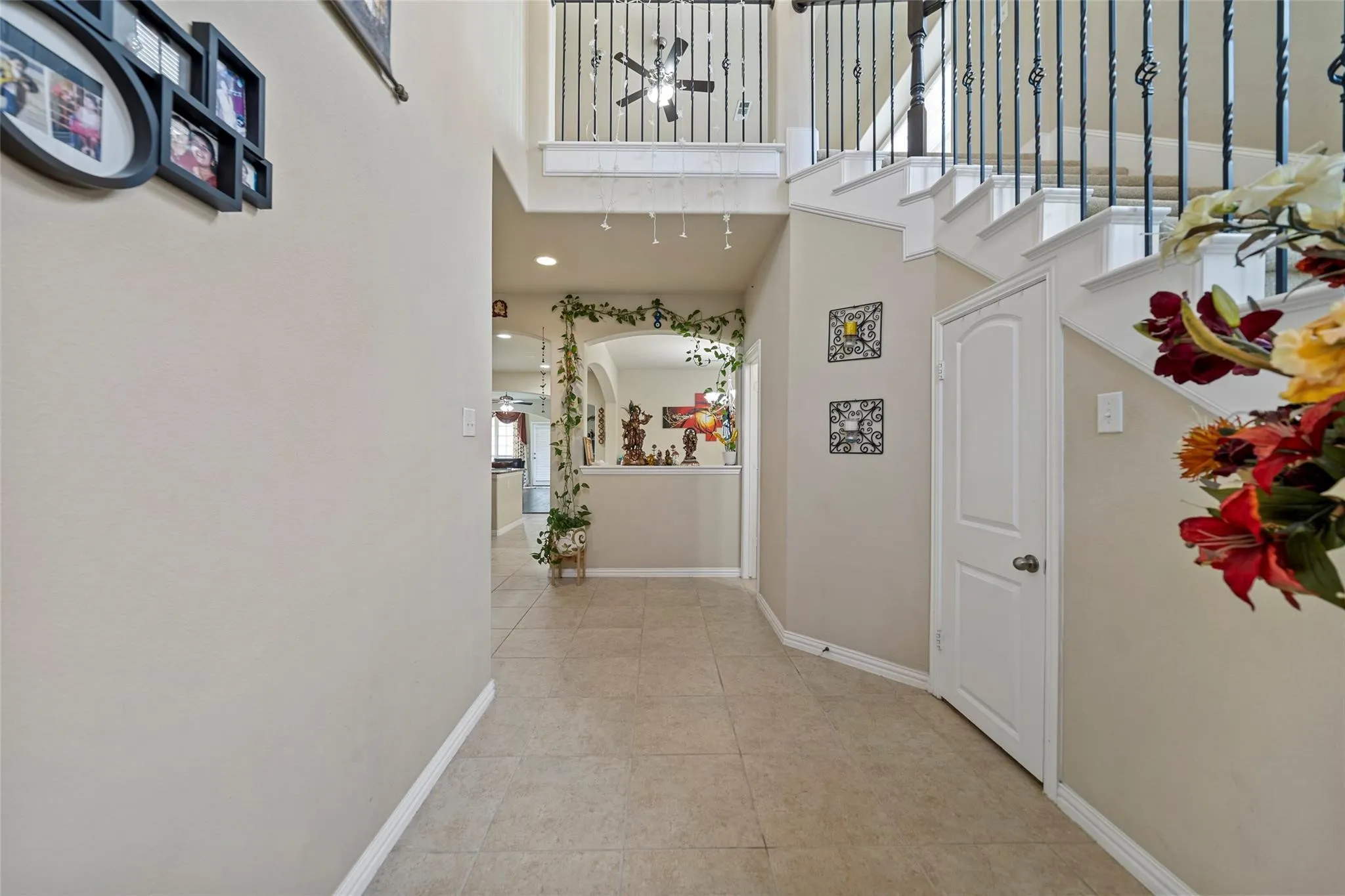 Two-story entry featuring ceramic tile flooring, a staircase with wrought iron balusters, and an arched hallway