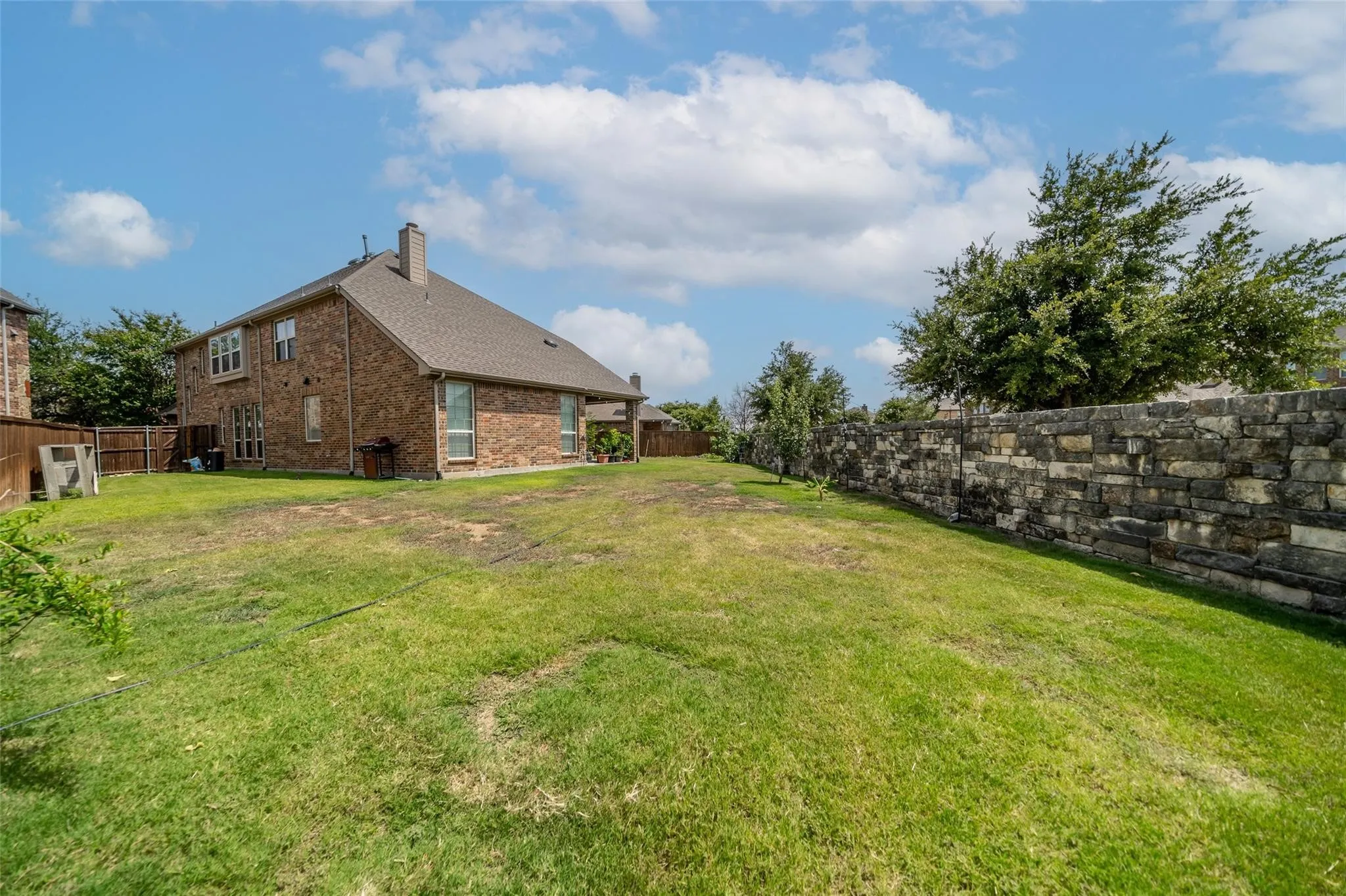 Expansive backyard featuring a stone retaining wall, mature trees, and a brick exterior