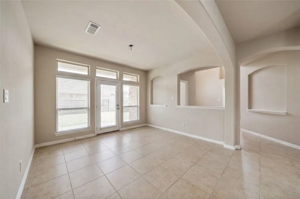 Tile flooring, multiple windows with blinds, arched wall openings, wall niches, and a glass-paneled exterior door