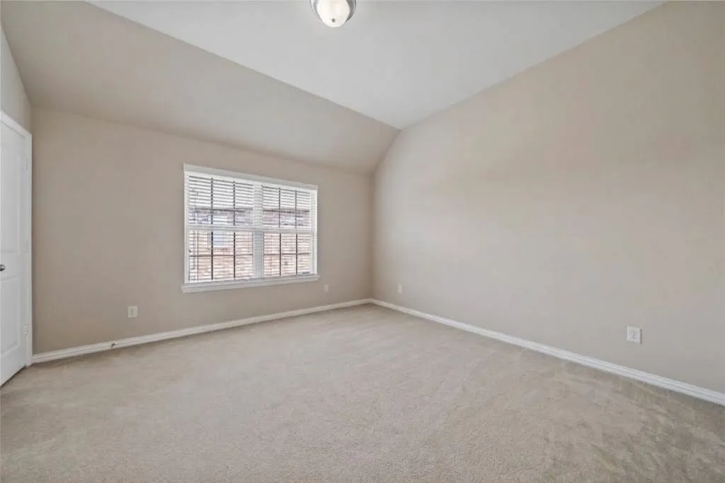 Carpeted room featuring neutral wall tones, a window with blinds, and a sloped ceiling