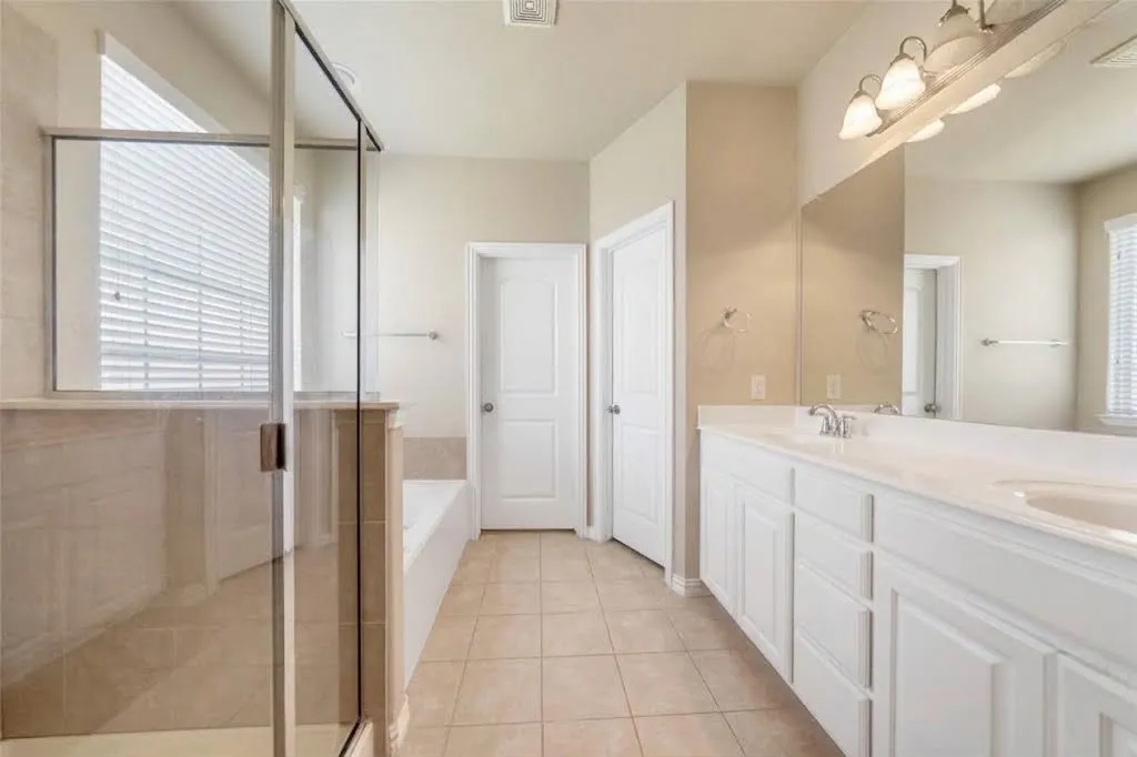 Dual vanity with undermount sinks, separate glass-enclosed shower, built-in bathtub, and tile flooring