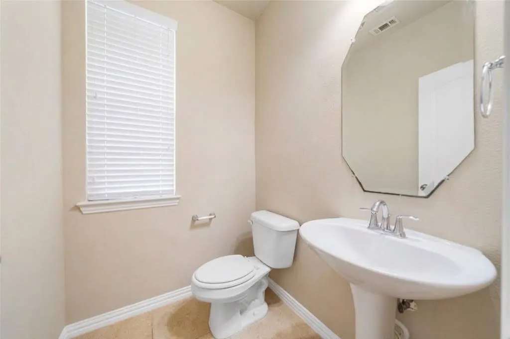 Pedestal sink with chrome faucet, octagonal mirror, window with blinds, and tile flooring