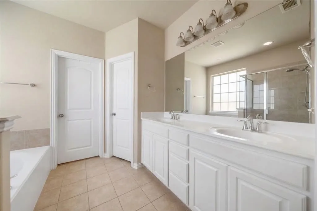 Dual vanity with white cabinetry and integrated sinks, large mirror, tiled flooring, glass-enclosed shower, and a built-in tub