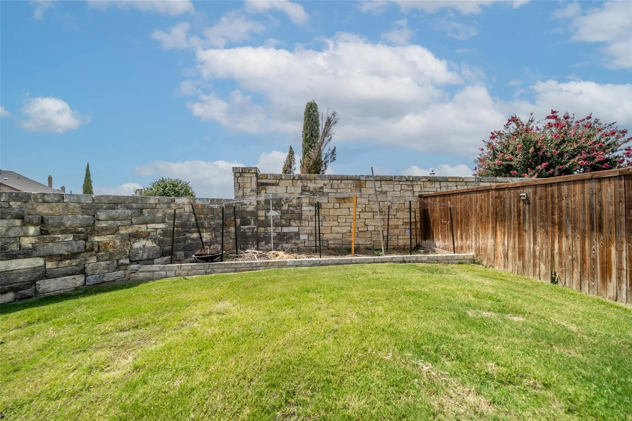 Expansive backyard space featuring a stone retaining wall and a wood privacy fence