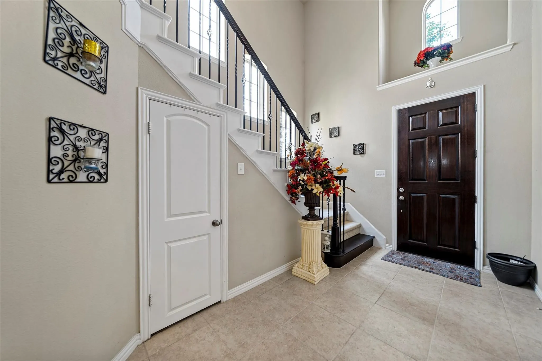 Two-story entry with tile flooring, a dark wood paneled entry door, and a staircase featuring wrought iron balusters