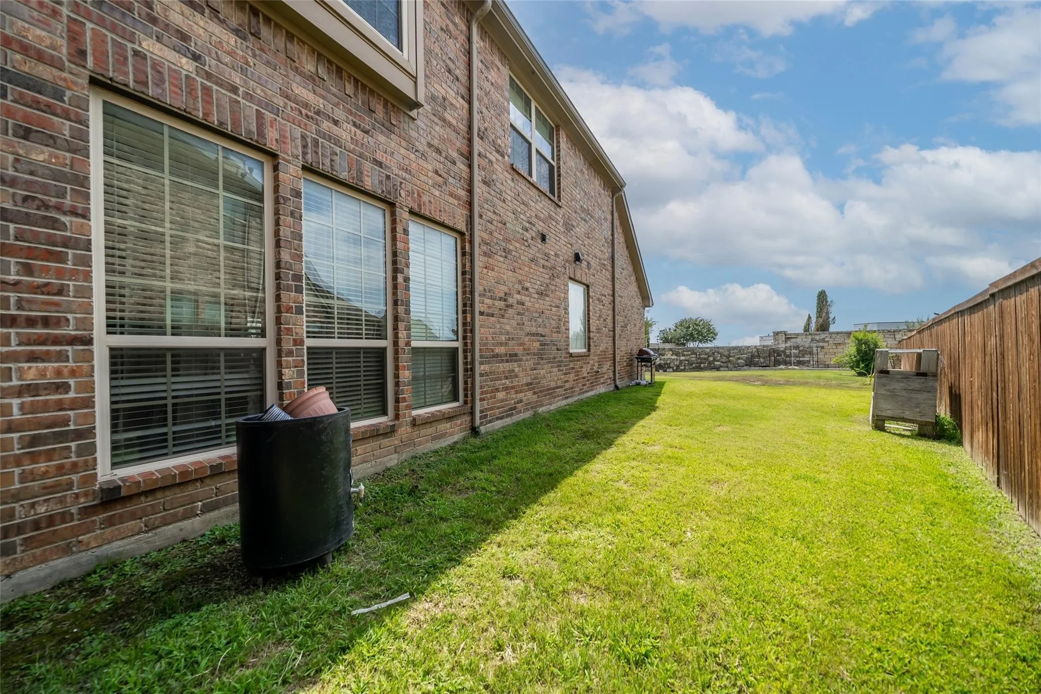 Brick exterior with multiple windows, wood panel fencing, and a stone retaining wall