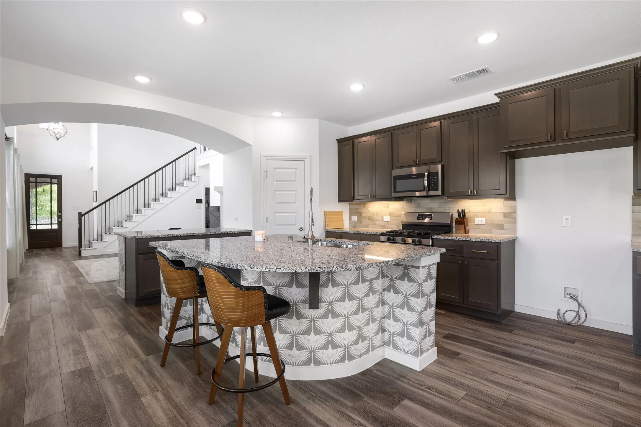 Kitchen featuring dark wood-finish cabinetry, stainless steel appliances, granite countertops, and a tile backsplash