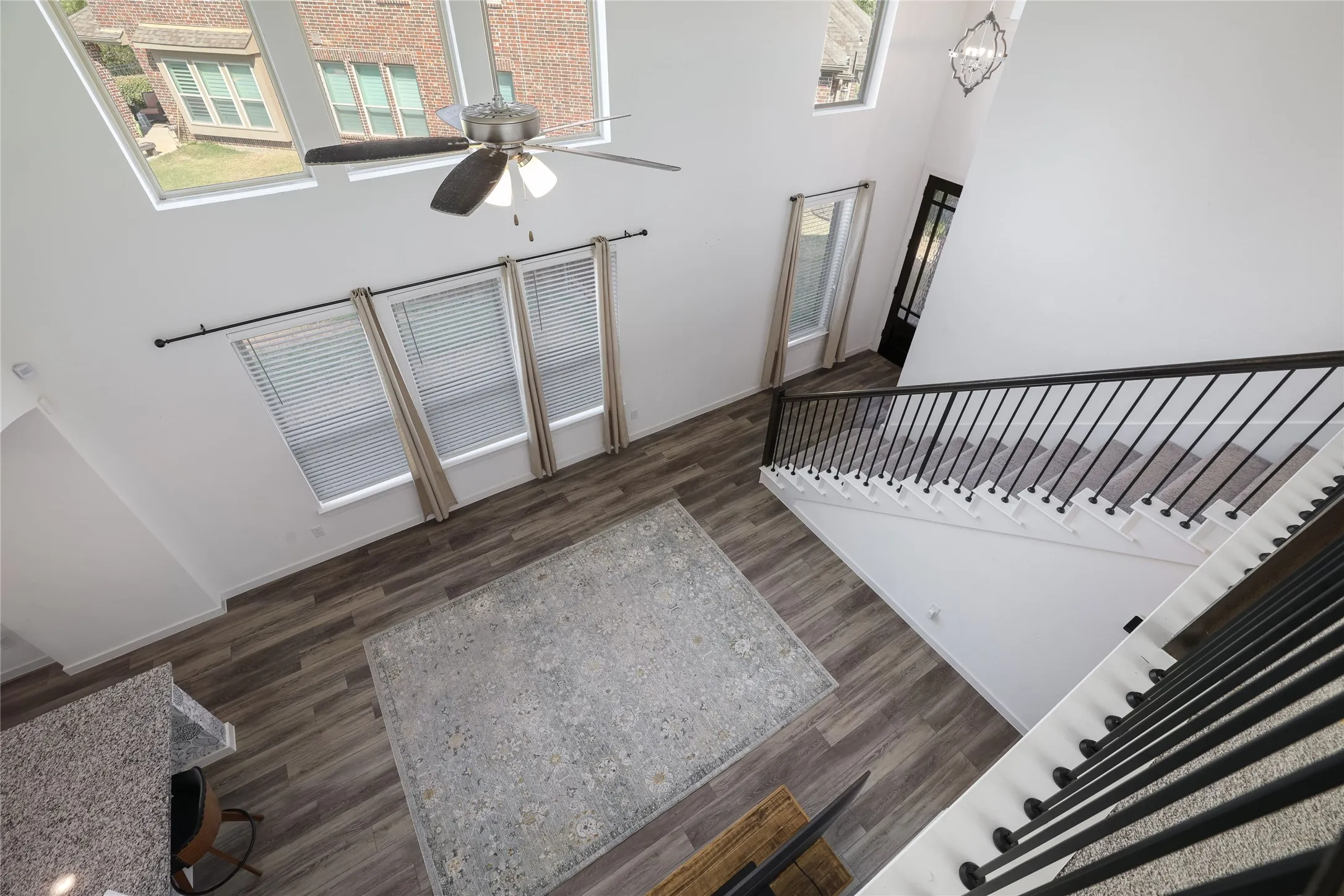 High ceilings with a ceiling fan, wood-finish flooring, multiple windows, a staircase with black iron balusters, and a black paneled door
